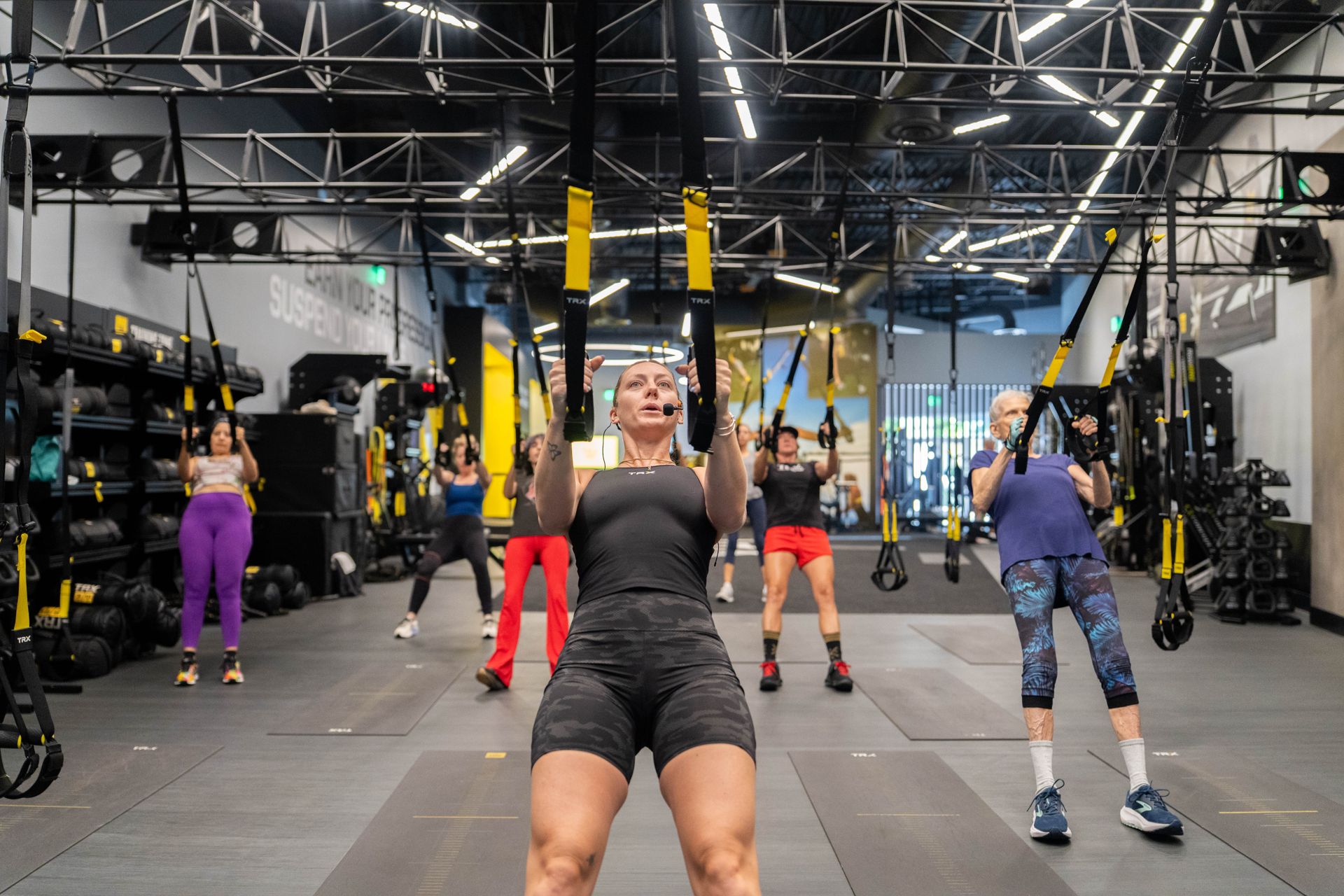 A TRX coach leads a small group class through suspension rows under the truss rig at TRX Training Center
